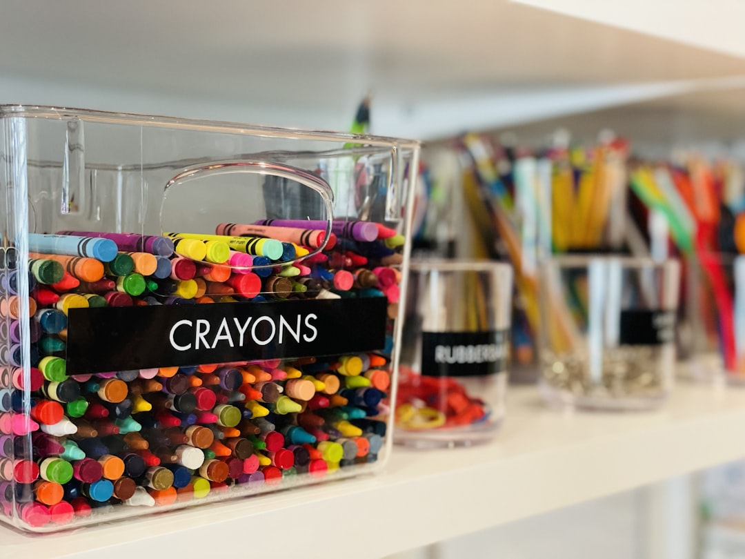 A clear plastic bin labeled "CRAYONS" filled with colorful wax crayons on a shelf
